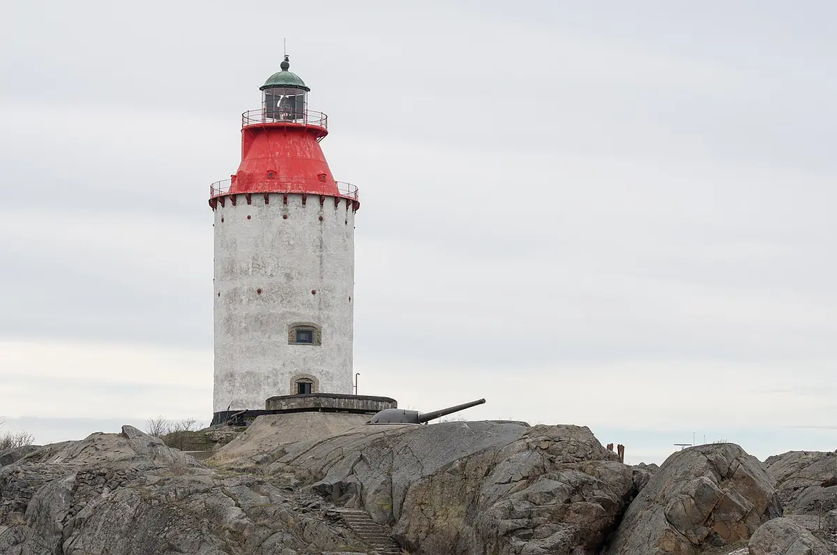 A white lighthouse with a red lantern room on bare rocks under a gray sky